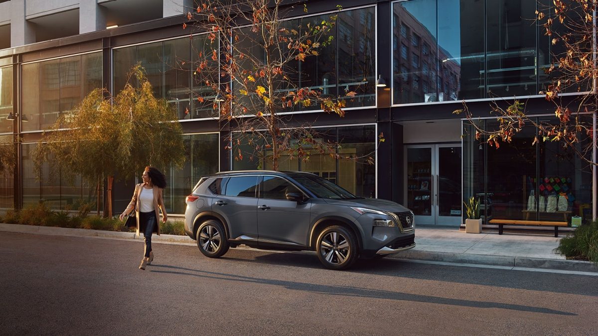 Vista lateral de camioneta SUV Nissan X-Trail 2025 con mujer caminando.