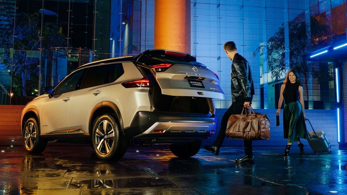 Vista trasera de SUV Nissan X-Trail e-POWER con pareja abriendo cajuela con sistema de apertura no touch con amplio espacio de almacenamiento.
